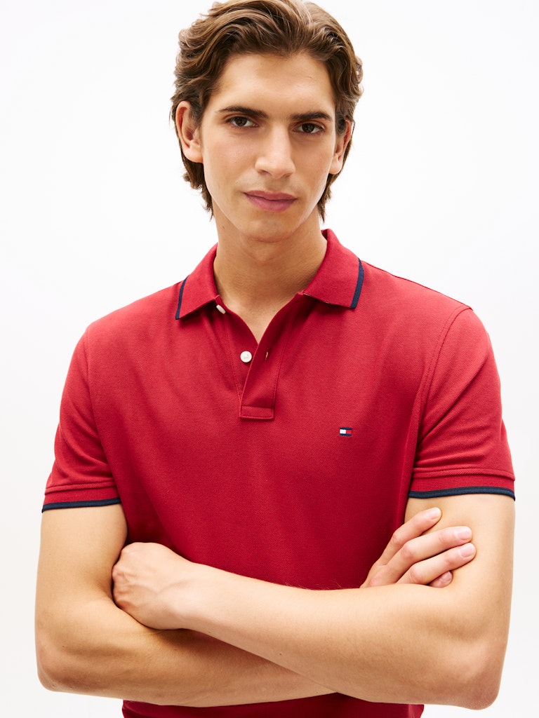 Man wearing a red polo shirt with a Tommy Hilfiger brand logo on a white background