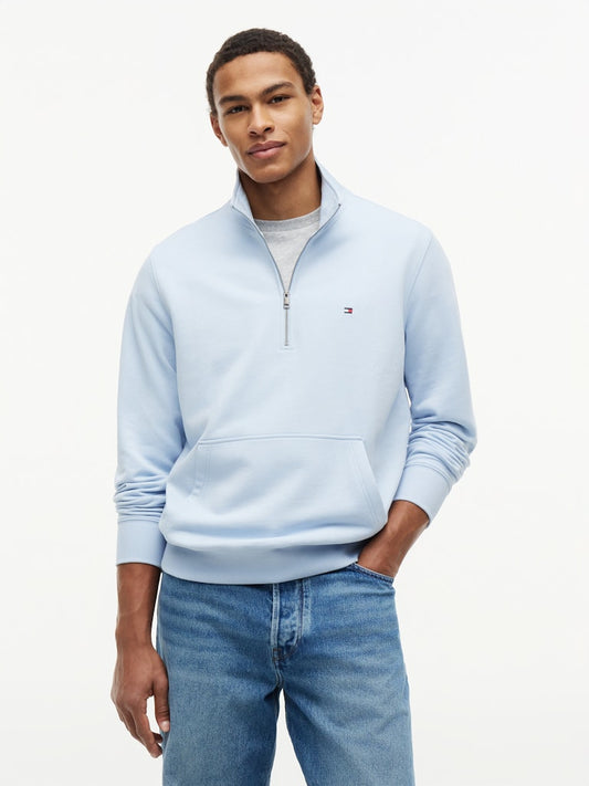 Man wearing a light blue sweatshirt with a Tommy Hilfiger logo on a white background