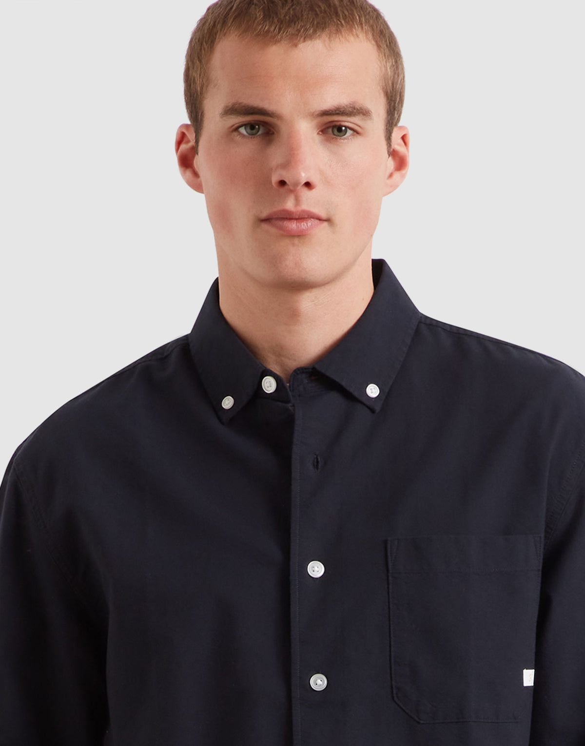 A man wearing a dark navy blue long-sleeve button-down shirt with a chest pocket, photographed against a light gray studio background.