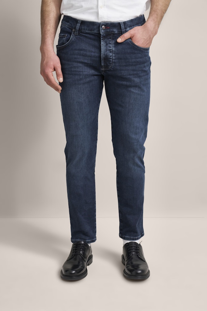 Person wearing blue jeans and black shoes on a plain background
