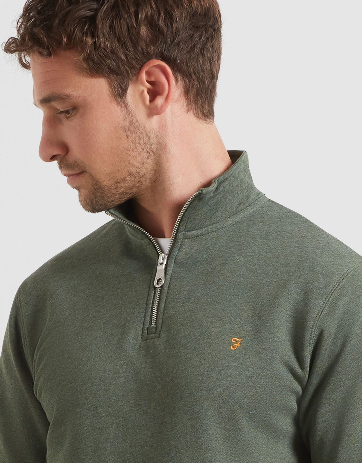 A man wearing a dark green heathered quarter-zip pullover sweater with a small gold F embroidered logo on the chest, shown in a close-up profile shot against a light gray background.