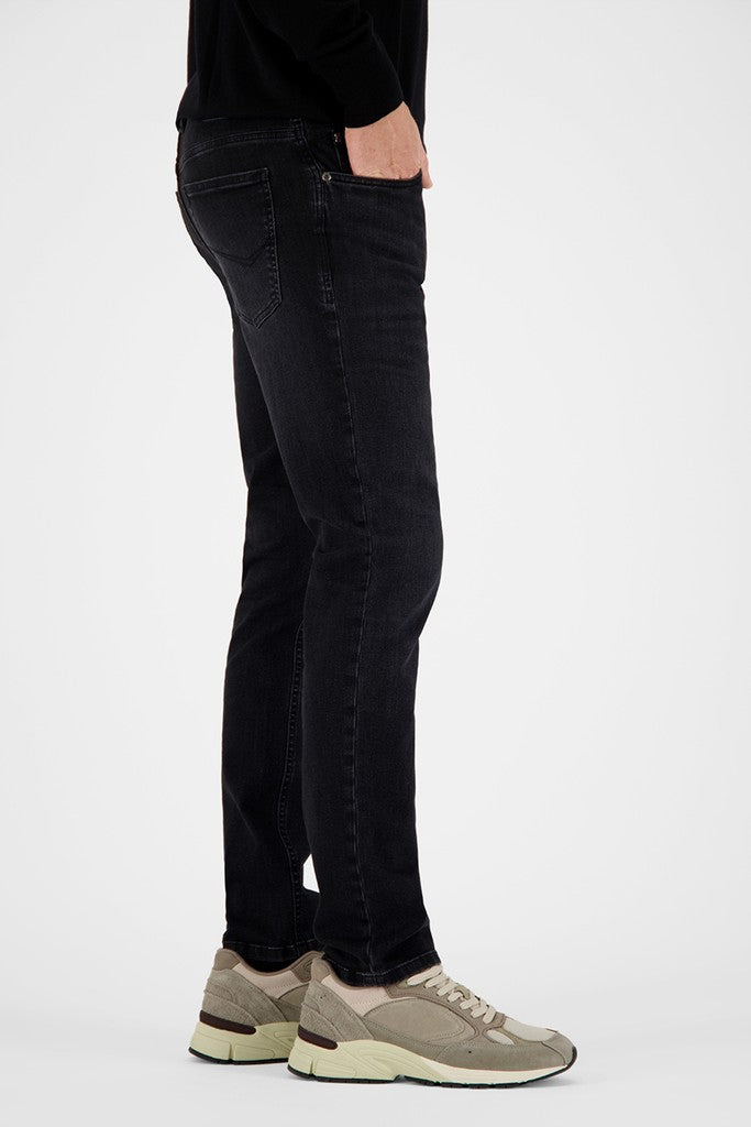 A side-profile view of a person wearing slim-fit black jeans and beige sneakers against a plain light gray studio background.