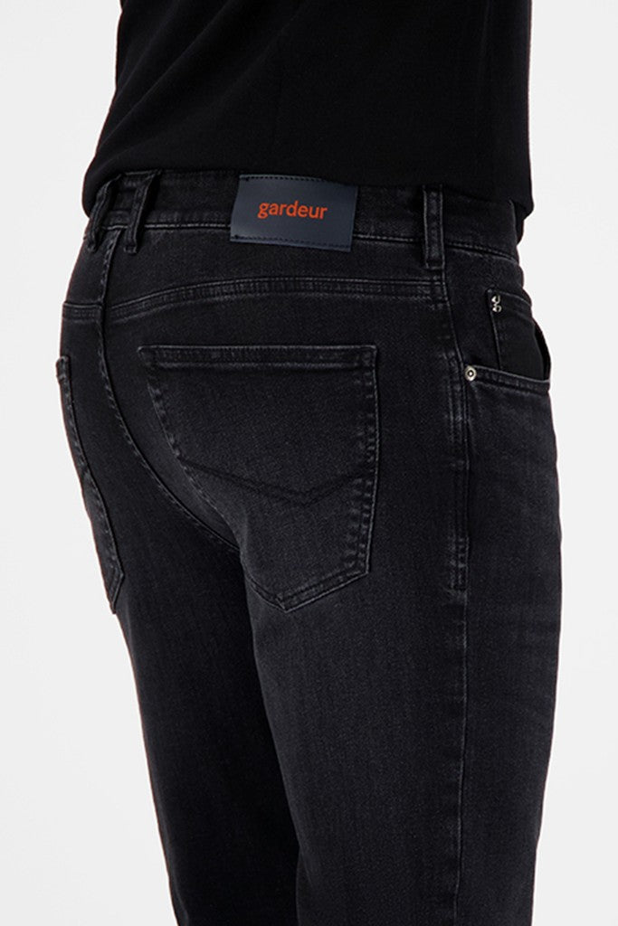 Close-up back view of a person wearing dark washed denim jeans with a black top. The jeans have a visible waistband patch reading 'gardeur' in orange text.