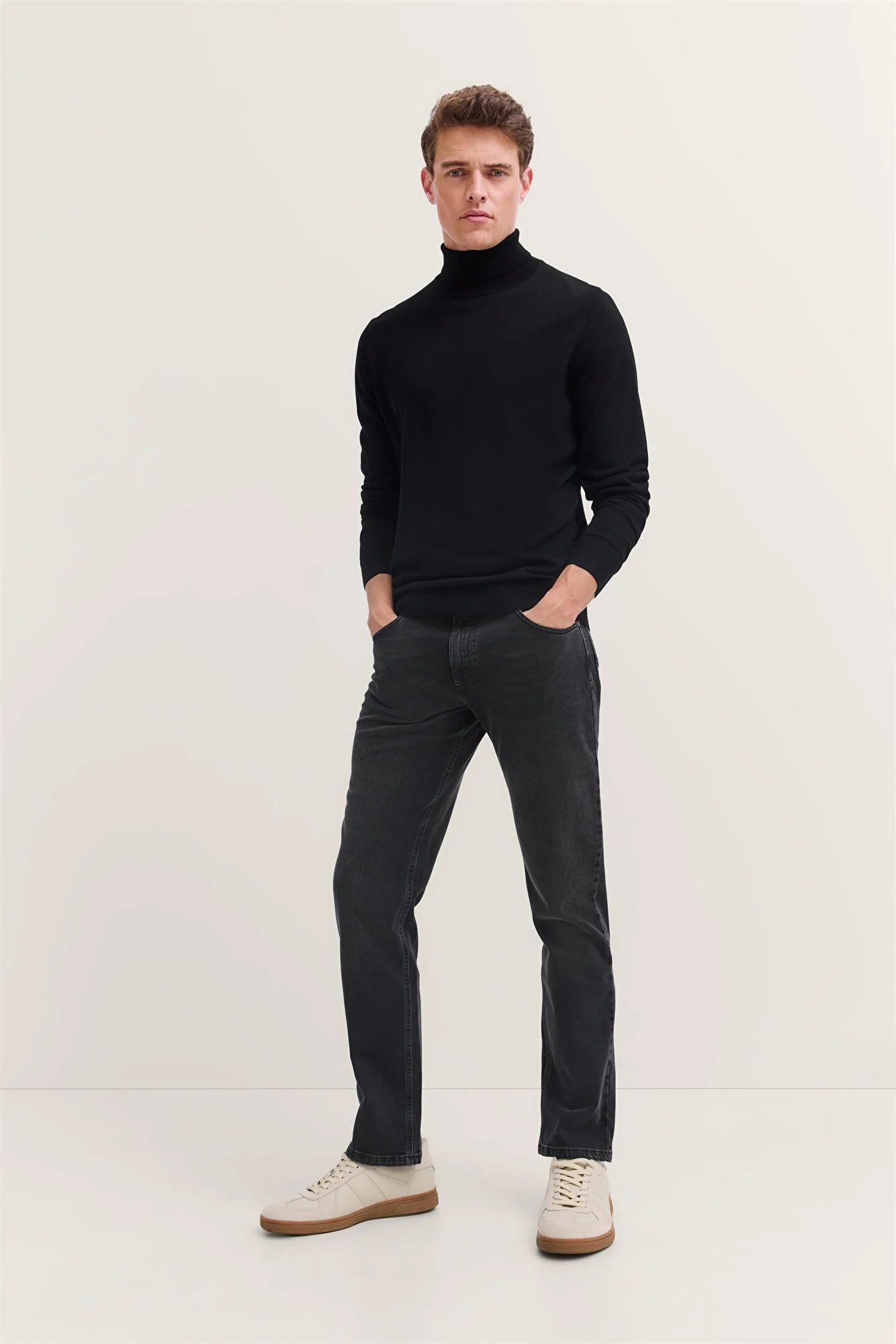 Man wearing a black turtleneck sweater and dark jeans on a white background