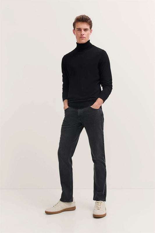 Man wearing a black turtleneck sweater and dark jeans on a white background