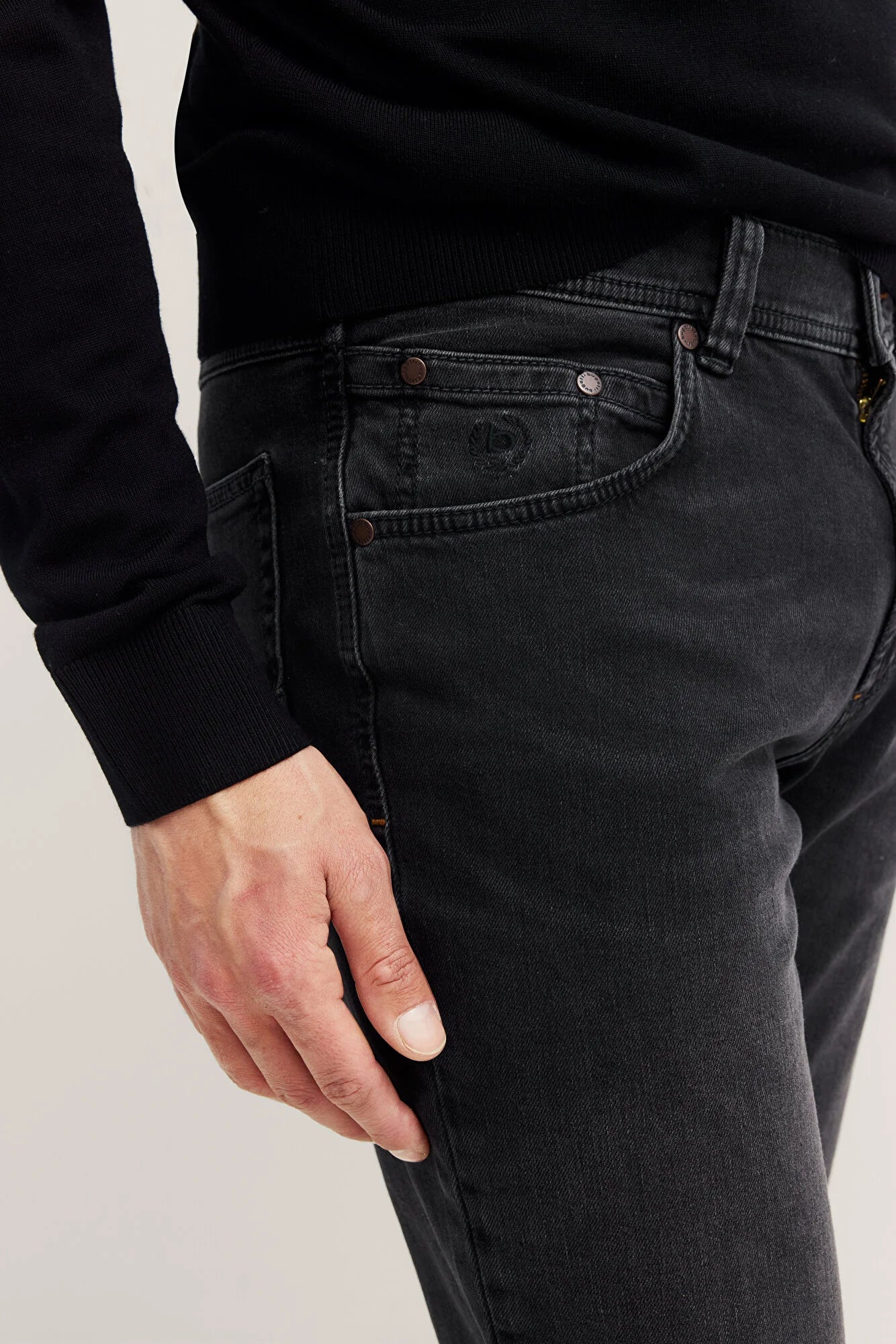 Person wearing black jeans with a Bugatti logo on a plain background