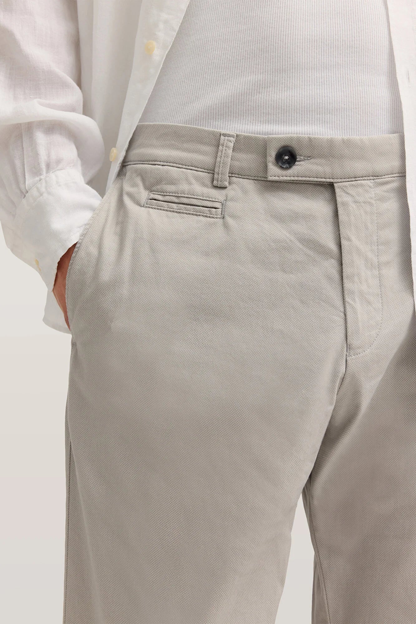 Close up of a man wearing light grey chinos and a white shirt with his hand in the pocket