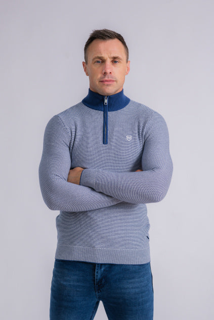 Tommy Bowe wearing a blue and gray patterned sweater with a quarter-zip design on a light gray background