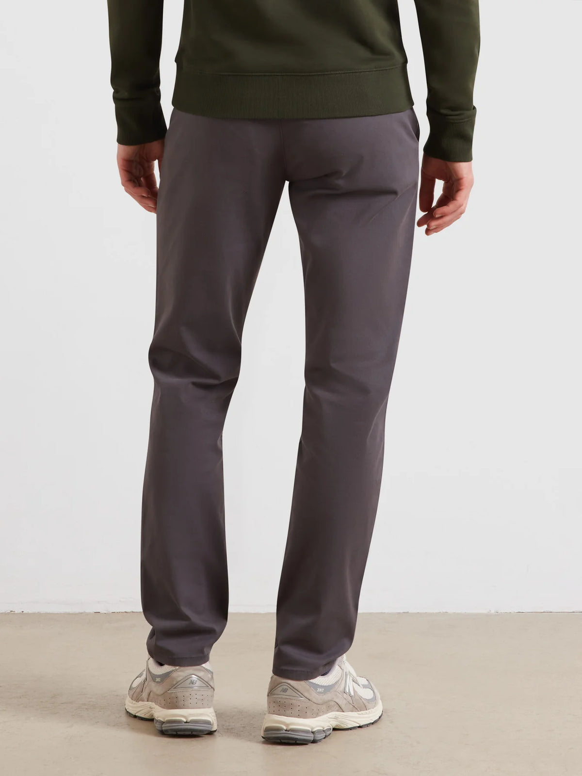 A person shown from the back wearing dark gray slim-fit pants, an olive green sweatshirt, and beige sneakers against a plain light gray studio background.